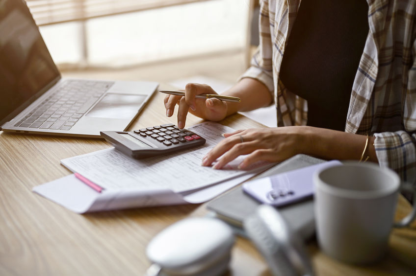 Close-up image of a woman using calculator, calculating money, managing household expenses and taxes in a living room.